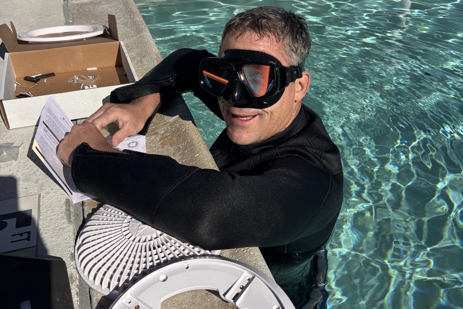 A technician in a wetsuit in the pool, fitting a new main drain cover